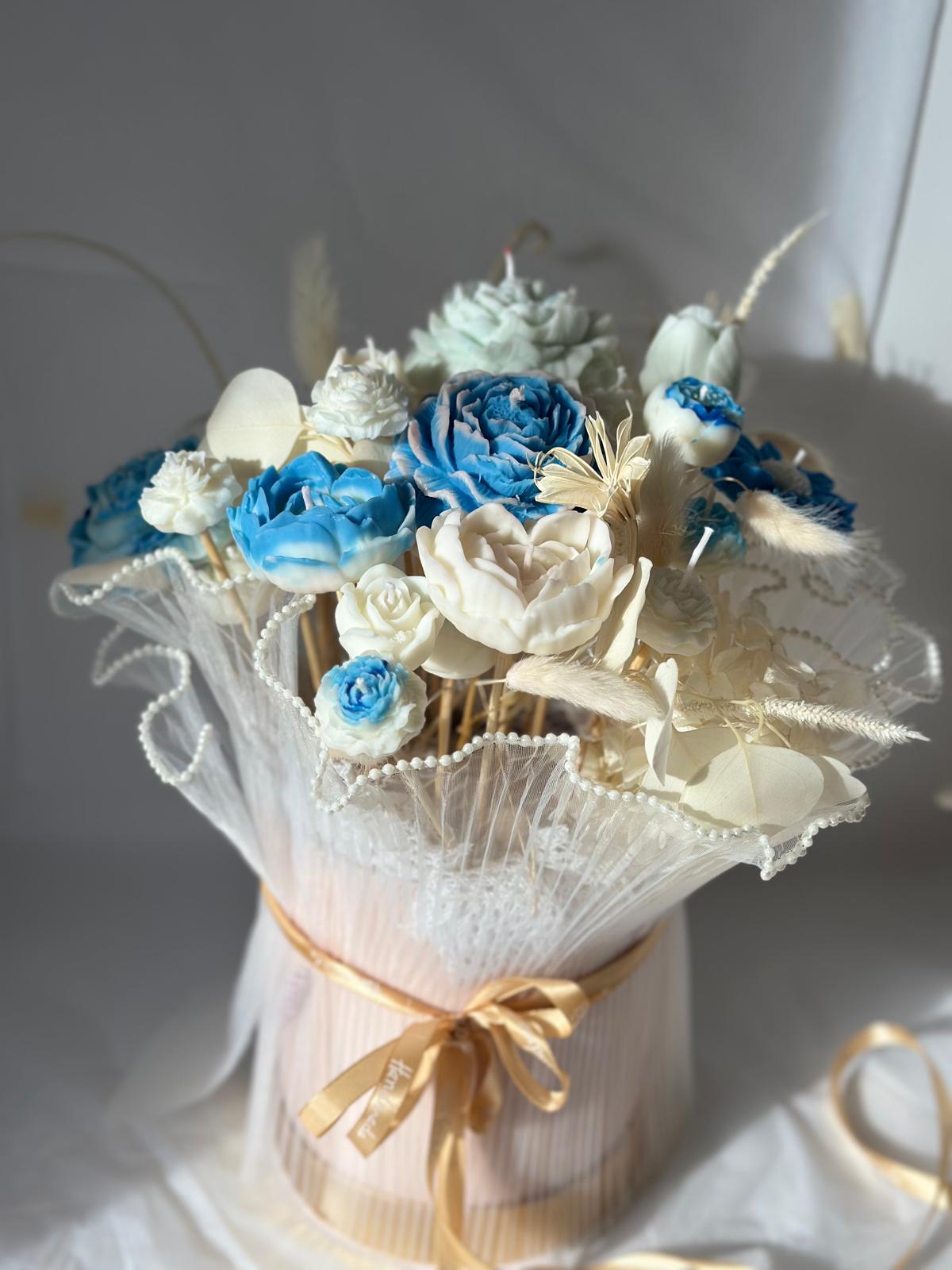 Mittelgroßer Kerzenstrauß mit blauen und cremeweißen Blütenkerzen, weißem Tüll und goldenem Band.