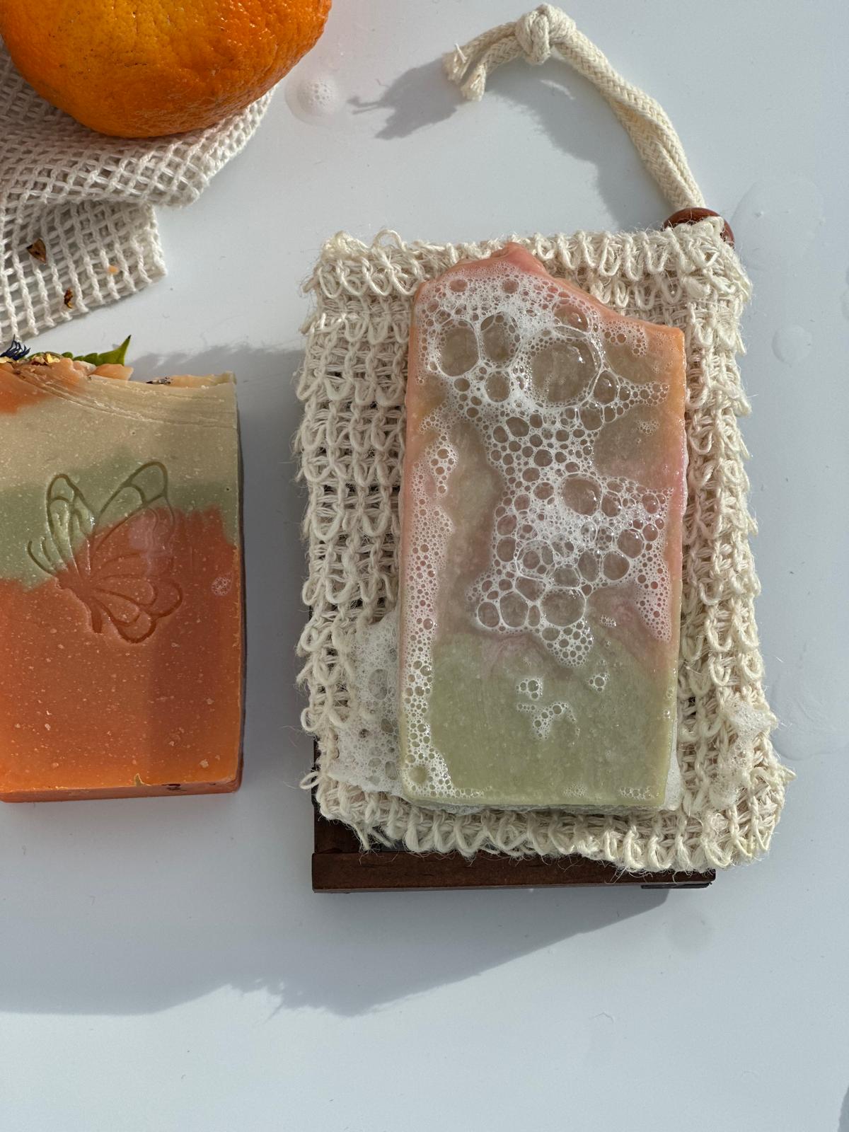 Nahaufnahme einer aufgeschäumten Orangenblütenseife auf einem Seifensäckchen neben einem zweiten Seifenstück.