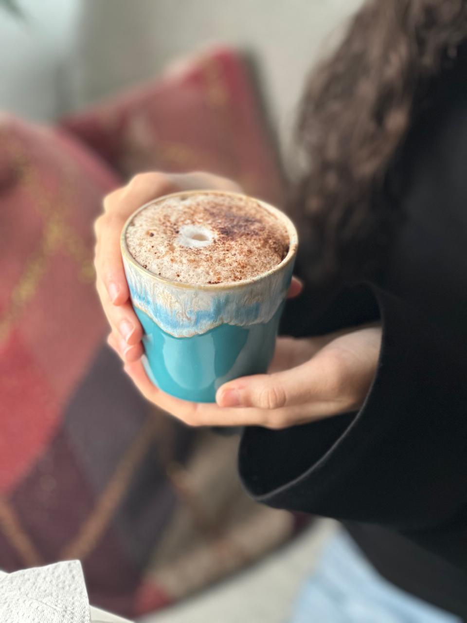 Türkiser Keramikbecher der Citrus Breeze Sojakerze, wiederverwendet für ein Kaffeegetränk und in beiden Händen gehalten