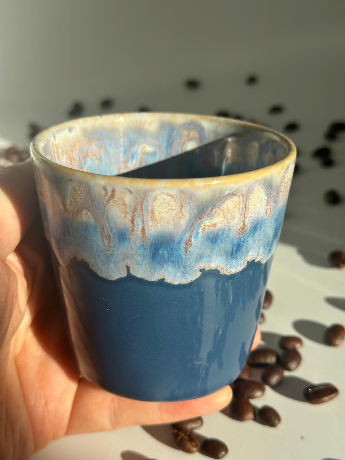 deep-sauvage-blauer-keramikbecher-Blauer Keramikbecher in einer Hand neben Kaffeebohnen