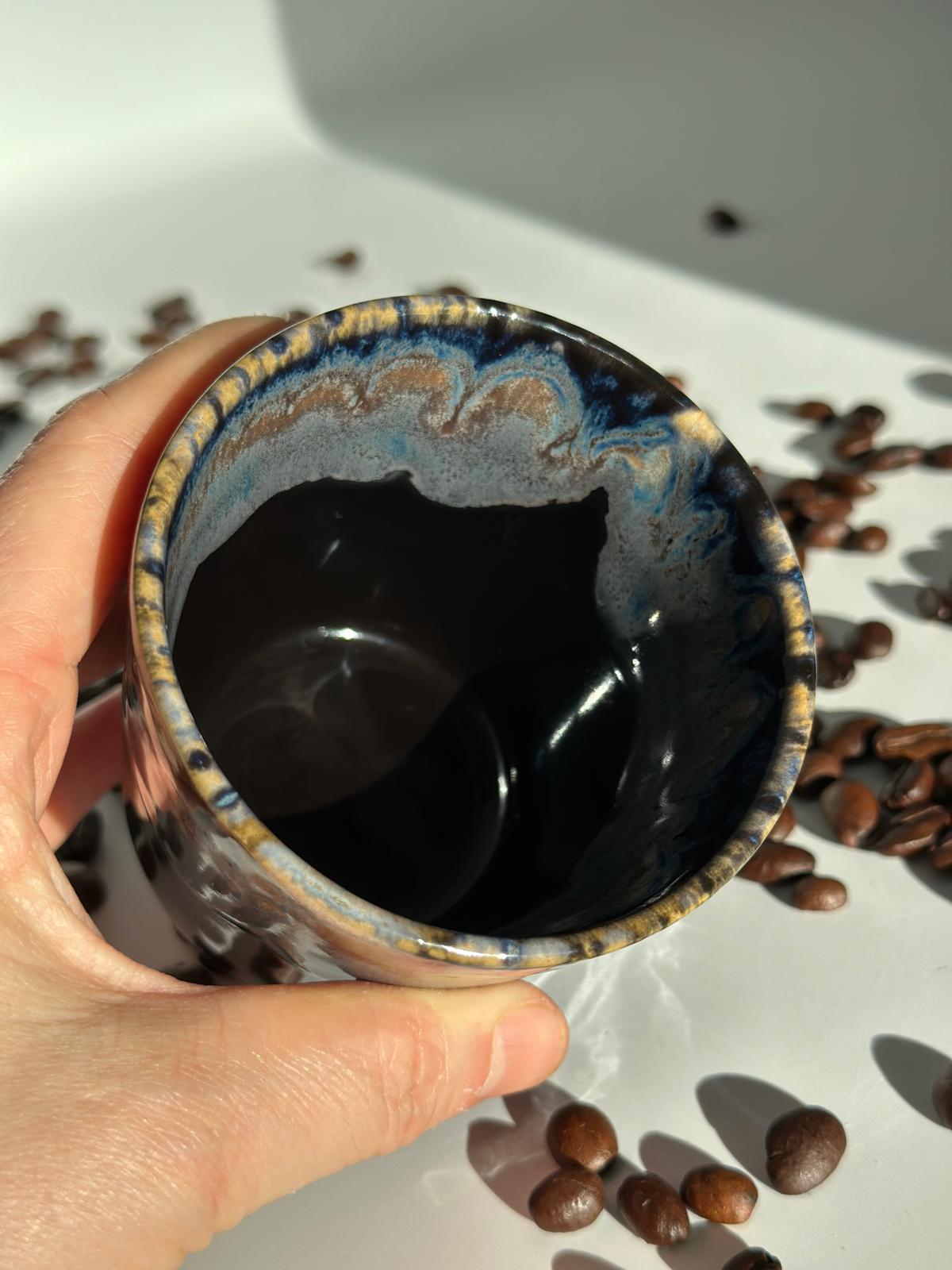 Wiederverwendbarer Keramikbecher der Midnight Blue Sojakerze, in einer Hand über Kaffeebohnen gehalten
